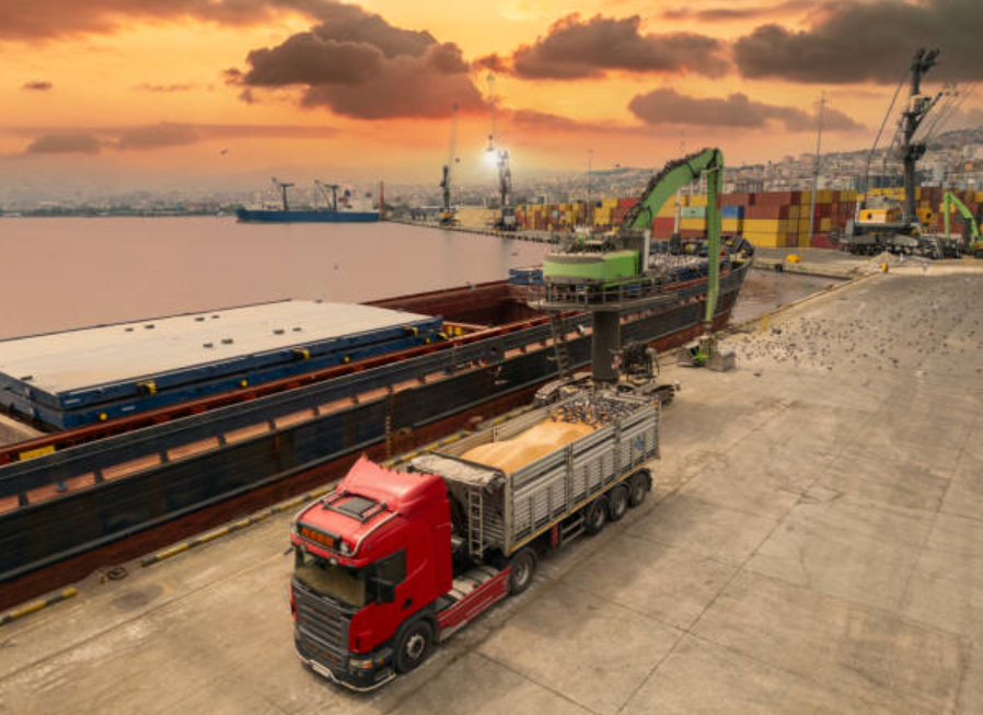 Red truck loading goods at a port during sunset, showing cross-docking in action.