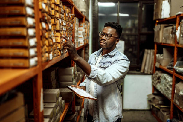 Worker checking inventory on warehouse shelves with clipboard in hand.