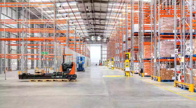 Large warehouse with tall storage racks, pallets, and material handling equipment.