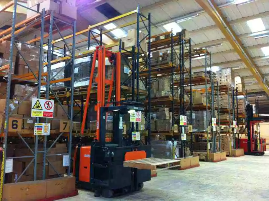 Large warehouse with tall storage racks, pallets, and material handling equipment.