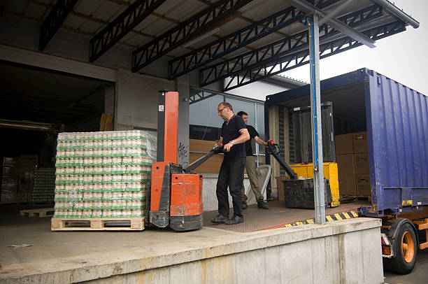 Workers unloading palletized goods from a shipping container at a warehouse dock.