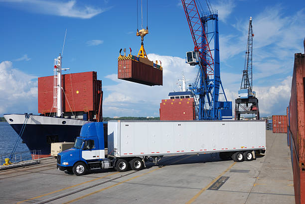 Transloading operation at a port with a container crane, cargo ship, and semi-truck.