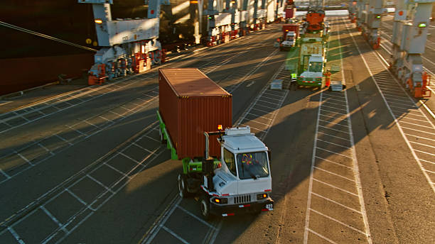 Truck transporting a shipping container at a busy port terminal.