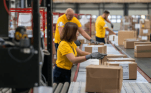 Employees sorting and preparing packages on a conveyor line inside a pick and pack warehouse.