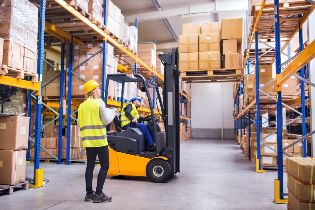 Busy pick and pack warehouse with workers using a forklift to move boxes along tall shelving aisles.