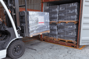  Forklift loading shrink wrapped pallets into a shipping container during restocking operations.