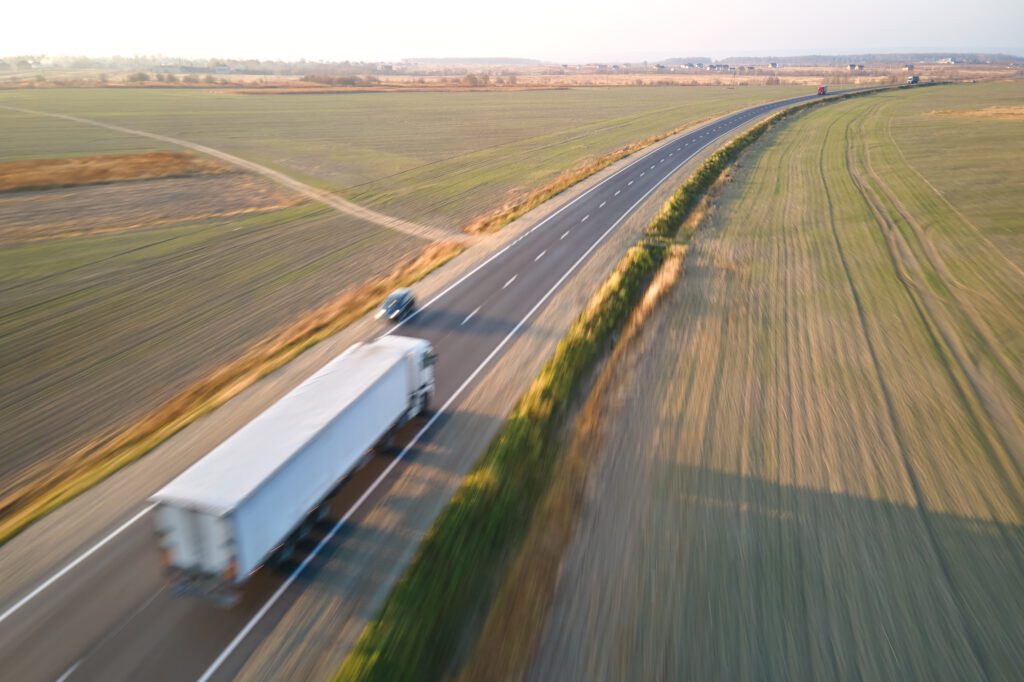 Aerial view of blurred fast moving semi-truck with cargo trailer driving on highway hauling goods in evening. Delivery transportation and logistics concept.